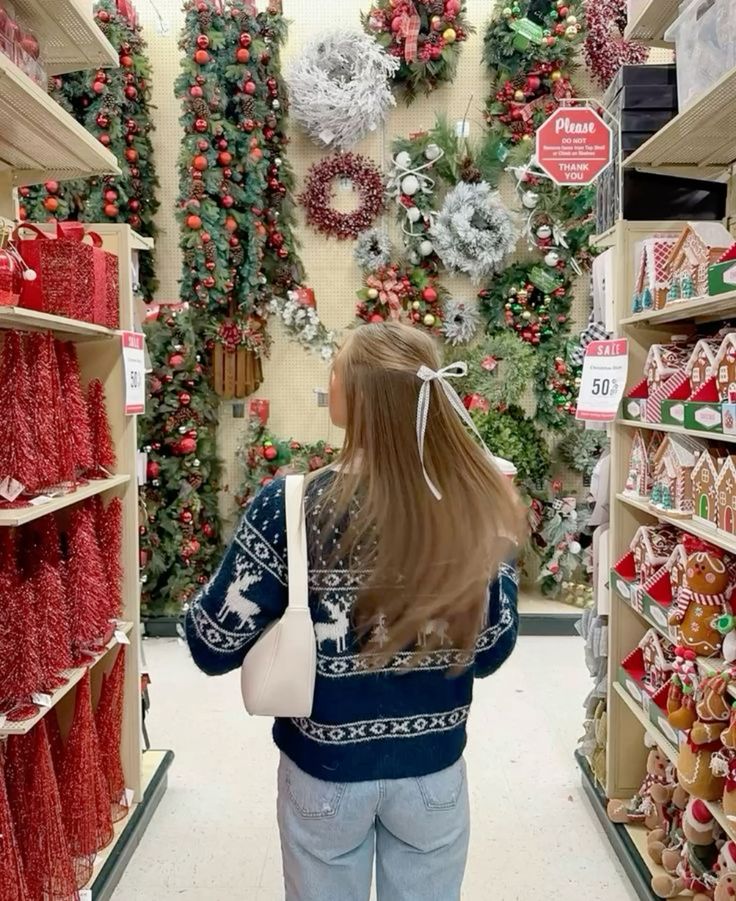 Hobby lobby Not mine - Handy Home Woman shopping for Christmas decorations in aisle of holiday wreaths and ornaments, wearing a festive sweater with reindeer design.