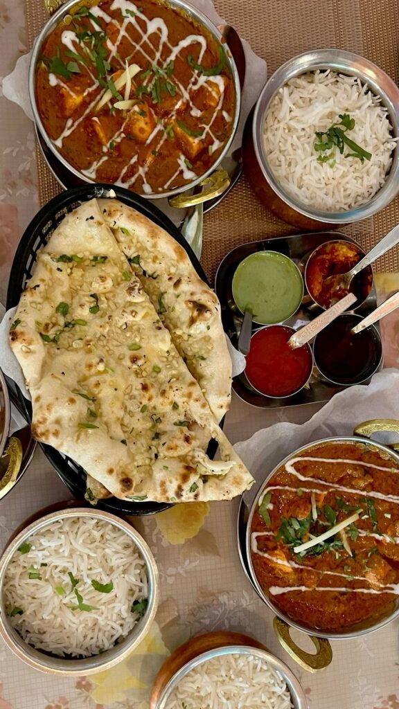 Indian food - Handy Home Delicious Indian meal with butter naan, fragrant basmati rice, paneer curry, and colorful chutneys on a dining table.
