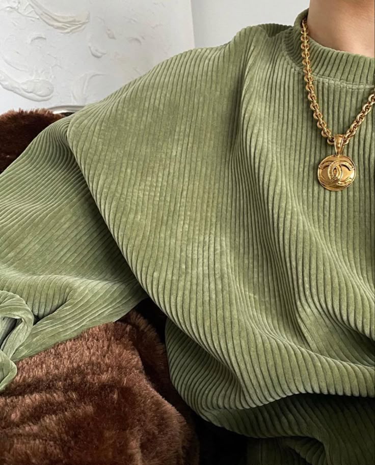 Person wearing a green ribbed sweater and a gold chain necklace with pendant, creating a cozy and stylish look.