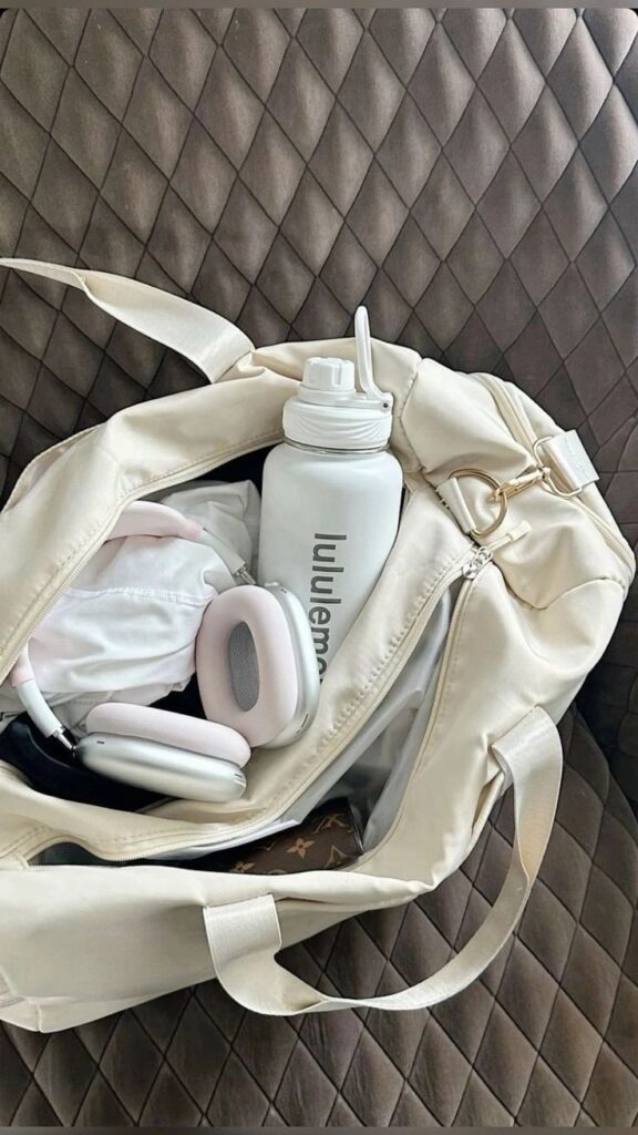 Lululemon fashion aesthetic white workingout - Handy Home Open beige gym bag on quilted surface, showing a water bottle, headphones, and clothing. Perfect for fitness enthusiasts on the go!