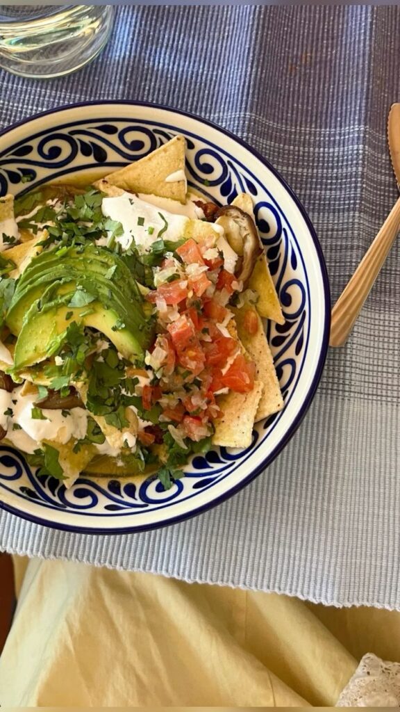 Mexican Nachos - Handy Home A vibrant dish of chilaquiles topped with avocado, salsa, and cilantro in a decorative bowl on a table setting.