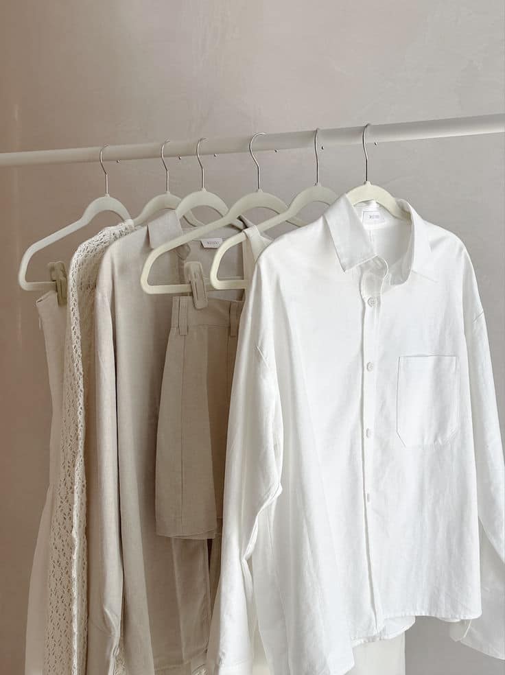 Minimalist neutral clothing on hangers: beige and white wardrobe essentials.