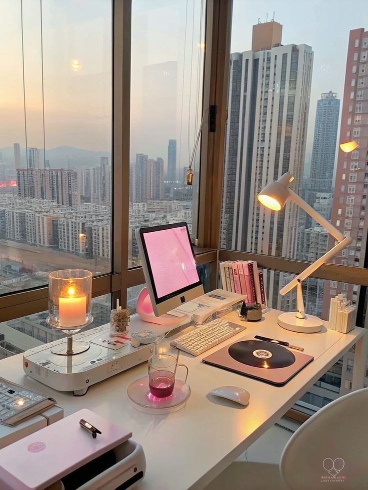 Modern home office setup with computer, pink accents, candle, and city view through large windows. Cozy and stylish workspace.