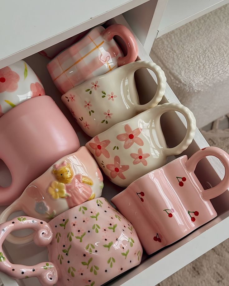 Assorted pastel mugs with floral and cherry designs neatly arranged in a drawer. Cozy, artistic kitchen decor.