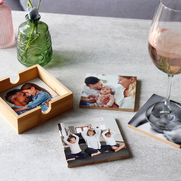 Family photo coasters on a table with a glass of wine and decorative vase, showcasing cherished moments and home decor elegance.