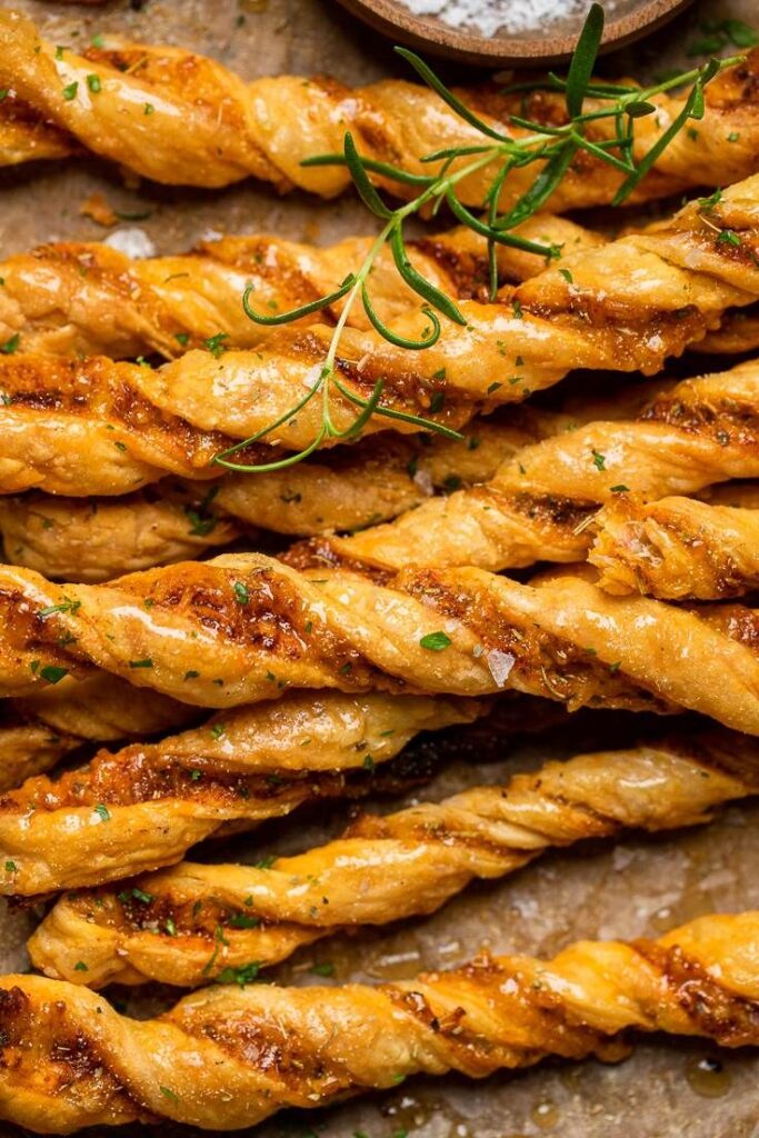 Sweet and Savory Vegan Cheesy Garlic Twists - Make - Handy Home Golden brown cheese twists garnished with herbs, perfect for appetizers or snacks. Delicious and crispy baked treats.