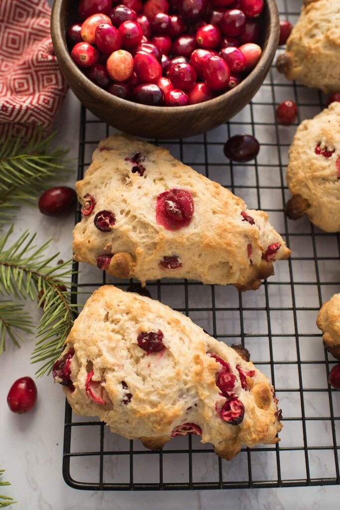 This easy scones recipe for Cranberry White - Handy Home Freshly baked cranberry scones on a cooling rack, with a bowl of cranberries, perfect for a festive treat.