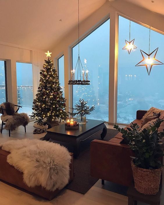 Cozy living room with Christmas tree, star lights, and large windows overlooking a snowy landscape, creating a festive ambiance.