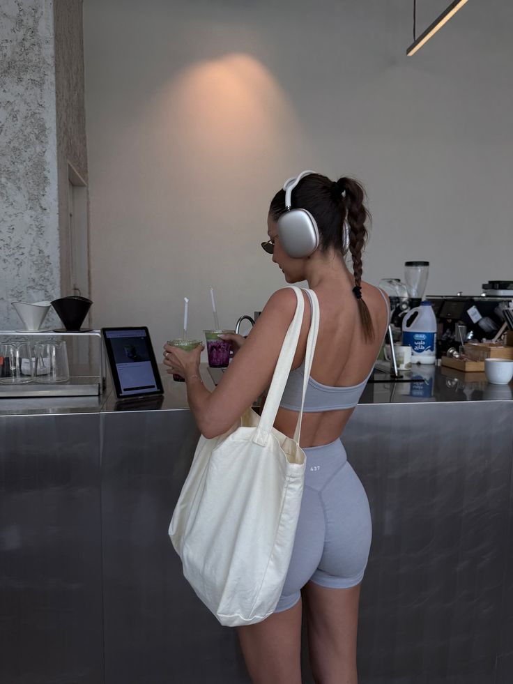 Person in workout attire with headphones and tote bag, picks up drinks from a cafe counter.