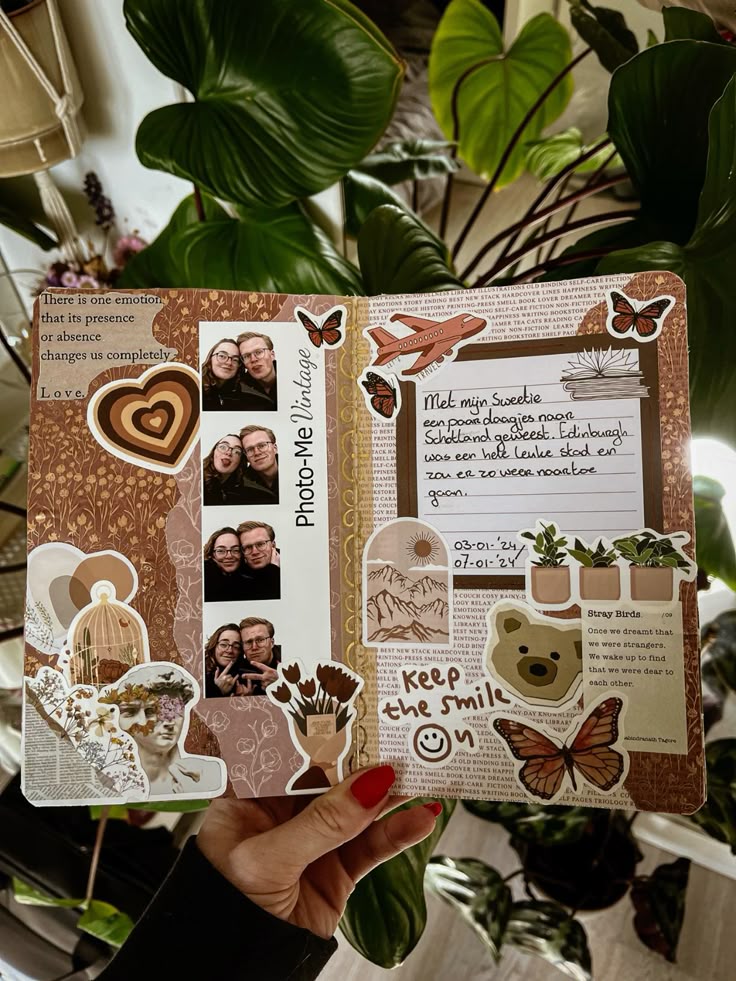 Vintage scrapbook open with photos, stickers, and handwritten notes, held by a hand with red nails. Lush plants in the background.