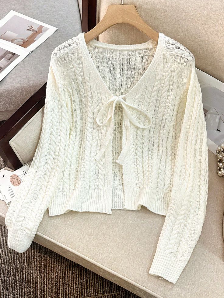 Cozy white knitted cardigan with tie-front detail on a hanger, perfect for winter fashion and layering elegance.