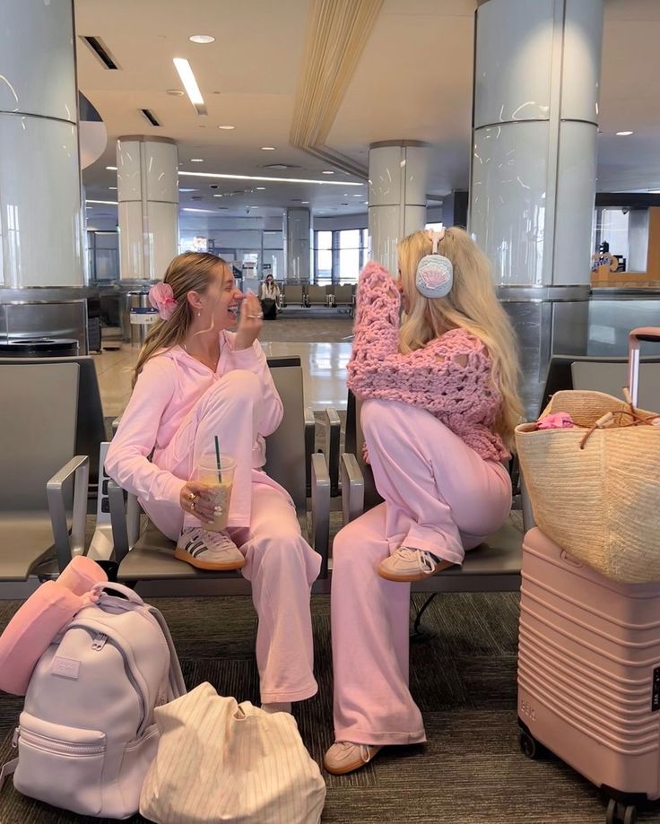 a25cfcb4-3cb2-49b1-8d4d-2ac371b3daf4 - Handy Home Two women in pink loungewear share a laugh at an airport, surrounded by stylish luggage and cozy accessories.