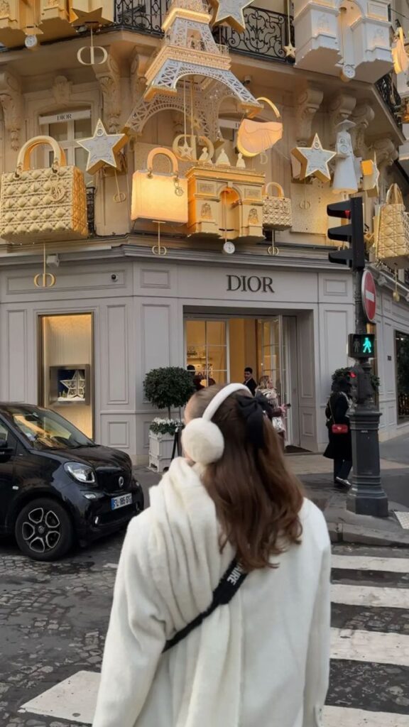 a5594bb9-9414-4795-a5b4-ddfa275589b0 - Handy Home Person in white coat admiring creative Dior storefront decor in Paris, featuring gold handbags and Eiffel Tower elements.