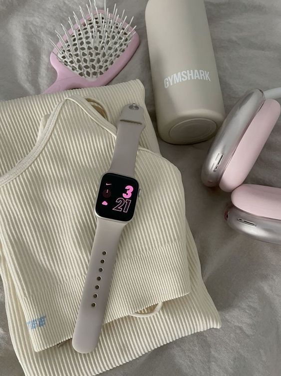 Fitness essentials: smartwatch, headphones, water bottle, brush, and workout clothes arranged on a bed for a gym-ready look.
