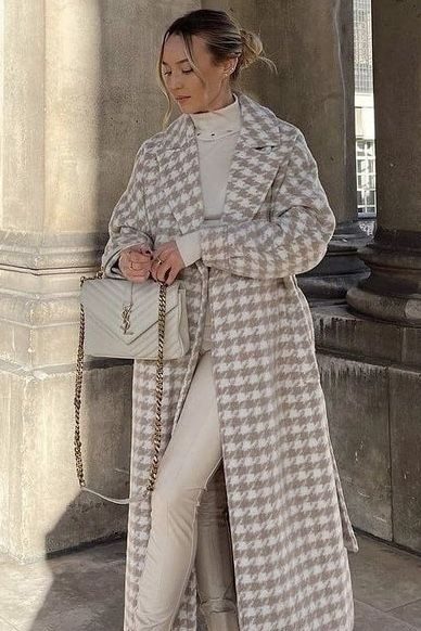 Woman in stylish houndstooth coat with beige boots and white handbag stands outdoors, exuding elegant fashion vibes.