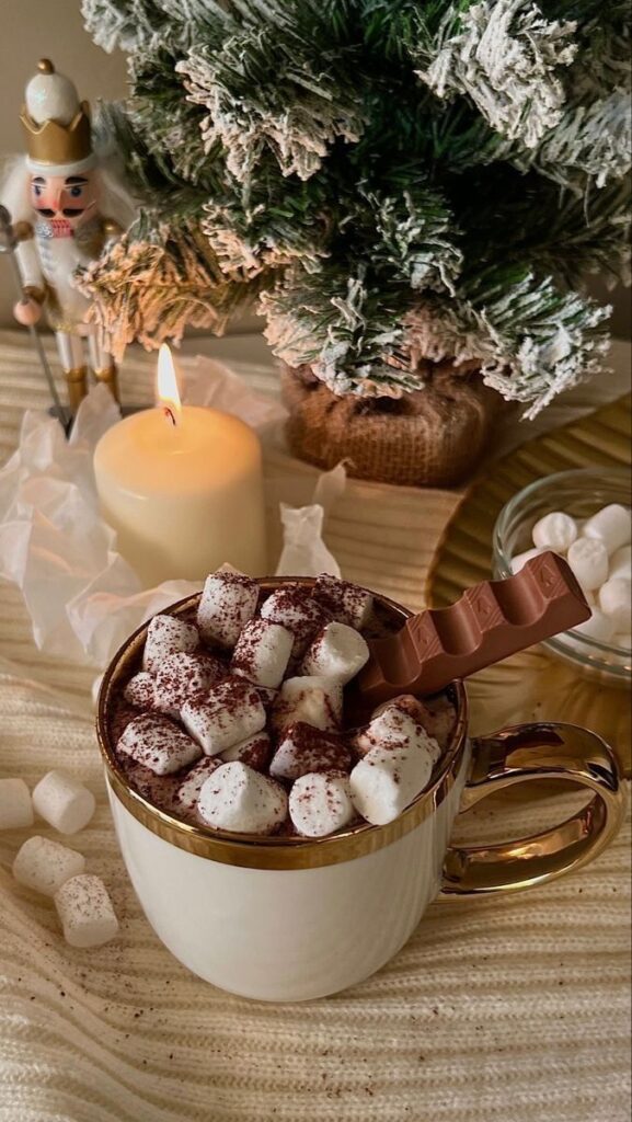 b4af76c2-0a57-4026-ab2c-31ebb5a47179 - Handy Home Creamy hot chocolate topped with marshmallows and chocolate, next to a lit candle and festive decor. Cozy winter treat.