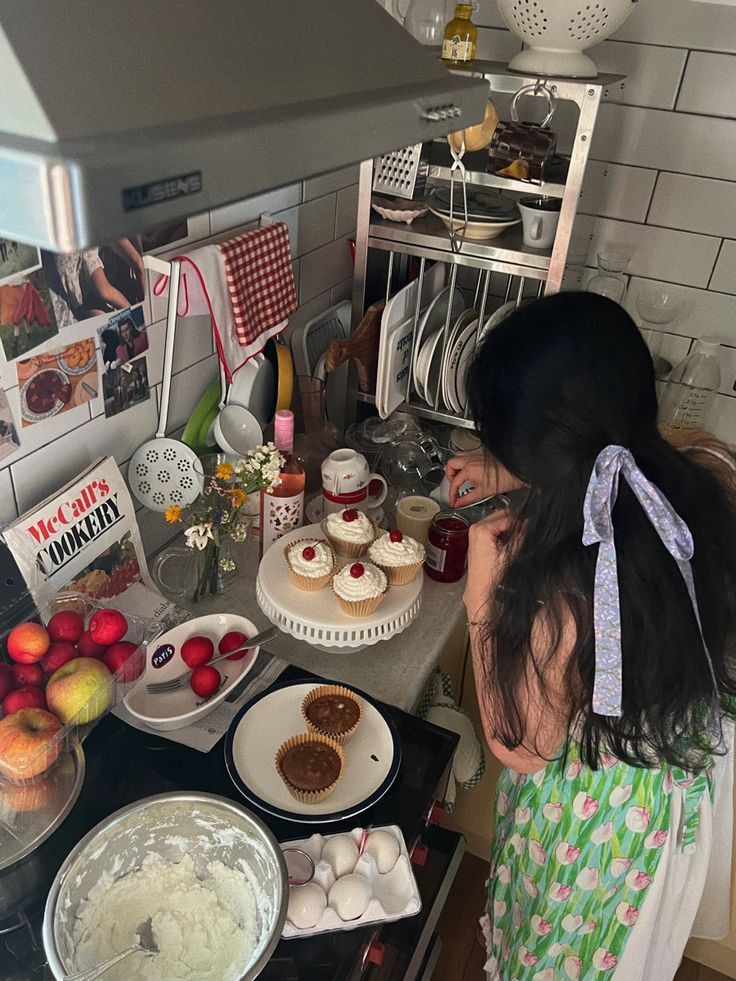 Woman decorating cupcakes in a cozy kitchen with fruit, flowers, and baking ingredients. Perfect for a homemade baking theme.
