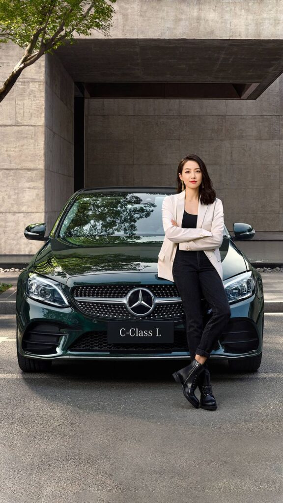 bd9b01c3-7655-42da-8547-b9e06c5ec83f - Handy Home Woman in white blazer leans on a Mercedes C-Class L car, modern background, showcasing luxury and confidence.