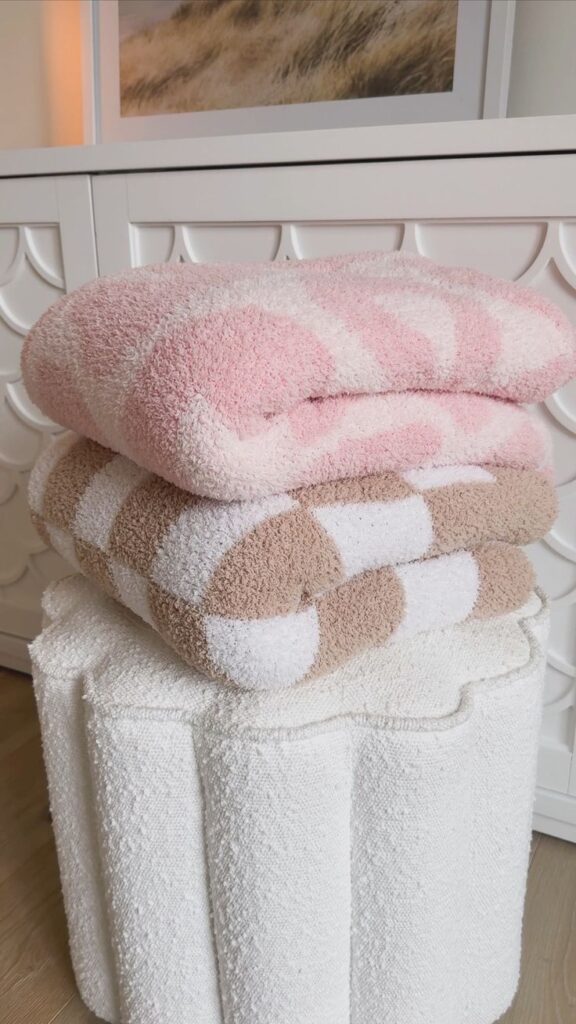 Soft pink and brown checkered towels neatly stacked on a textured white stool, perfect for cozy home decor.