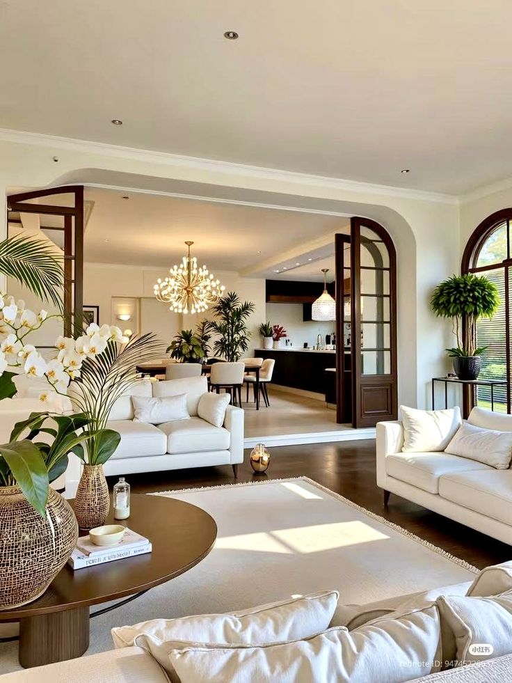 Luxurious open-concept living room and dining area with elegant decor, lush plants, and a grand chandelier.
