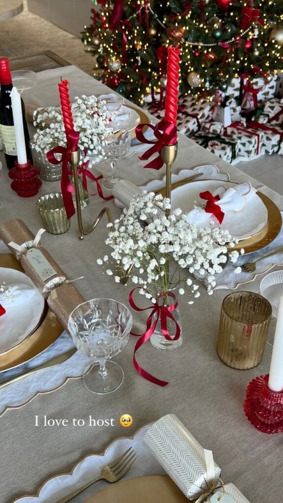 ea3b091b-bacc-404a-93c7-1c9aac138142 - Handy Home Elegant Christmas dining table with red candles, white plates, and a decorated tree in the background. Perfect for festive hosting!