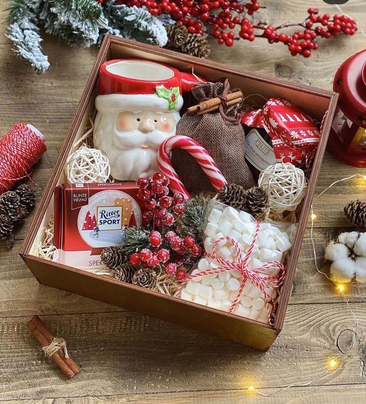 eefbe7ed-72b4-4b5b-af5f-a84bf994d2d0 - Handy Home Festive Christmas gift box with Santa mug, candy cane, chocolate, and holiday decor on a wooden table. Cozy holiday vibes.