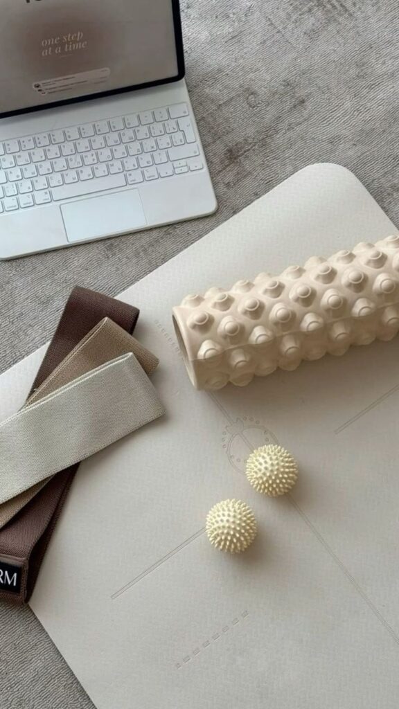 Laptop on a yoga mat with massage roller, spiky balls, and resistance bands; workout setup for home exercise.