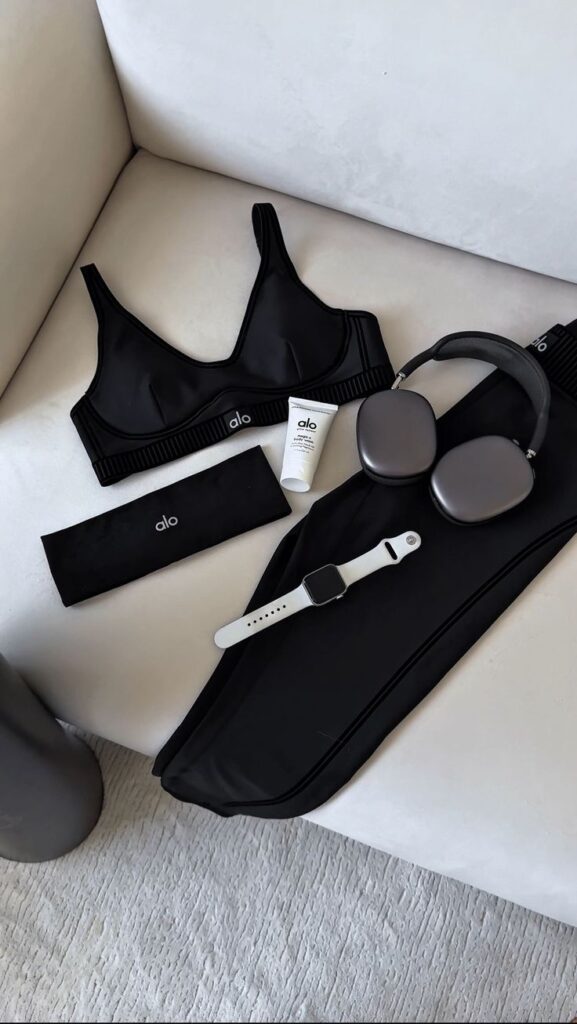 fabe0cc1-6b37-4b77-837c-558bbaa9abd2 - Handy Home Black workout wear, sports bra, leggings, headband, skincare, smartwatch, and headphones on a white sofa. Fitness essentials display.