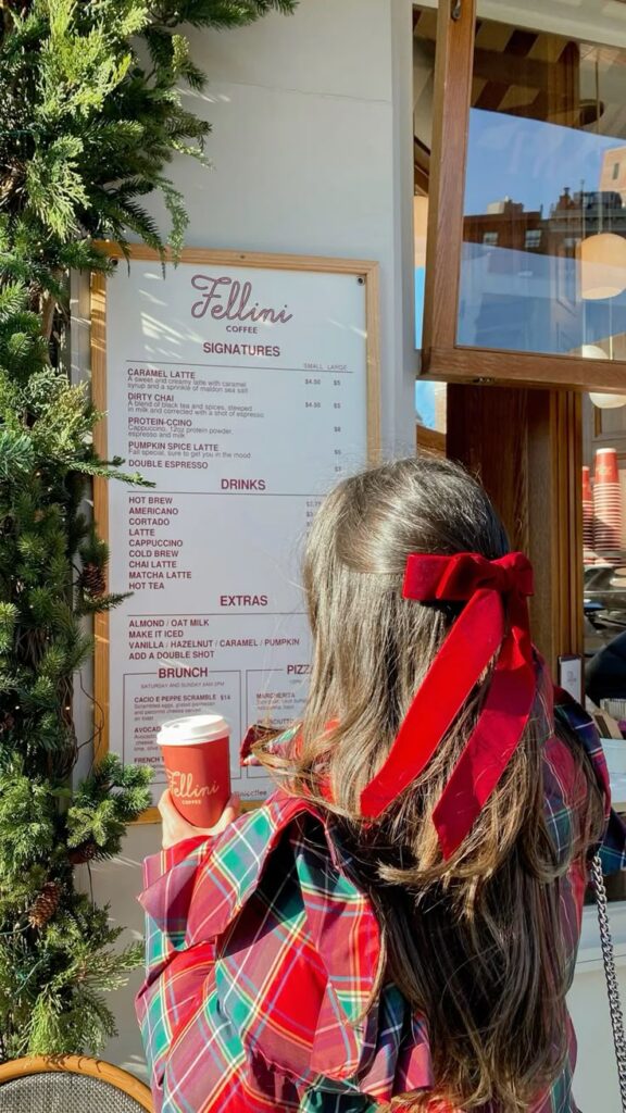 gabrielavasci - Handy Home Woman in plaid with red bow orders coffee at Fellini café, menu and festive decor visible. Cozy holiday scene.