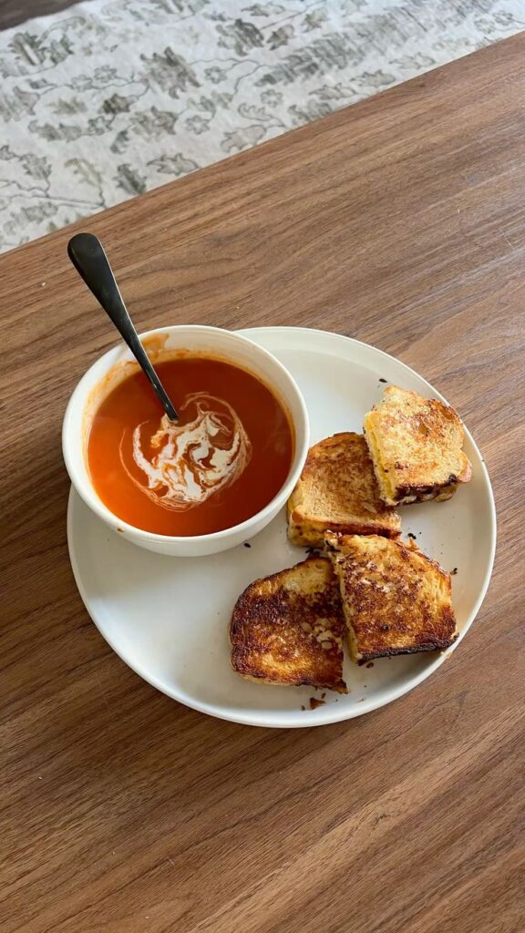 grilled cheese and tomato soup - Handy Home Creamy tomato soup with a swirl of cream, served with crispy grilled cheese sandwiches on a wooden table. Perfect comfort food.