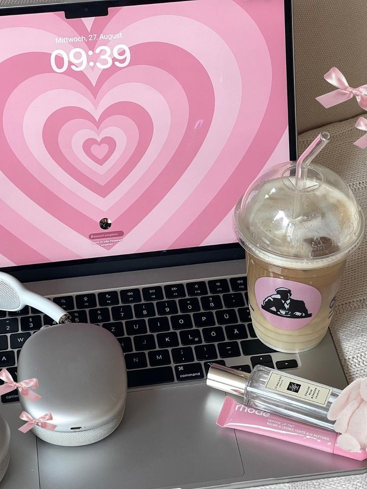 heres how I make my pinterest life happen and - Handy Home Laptop with pink heart wallpaper, iced coffee, perfume, lip tint, and headphones on keyboard. Cozy and stylish workspace.