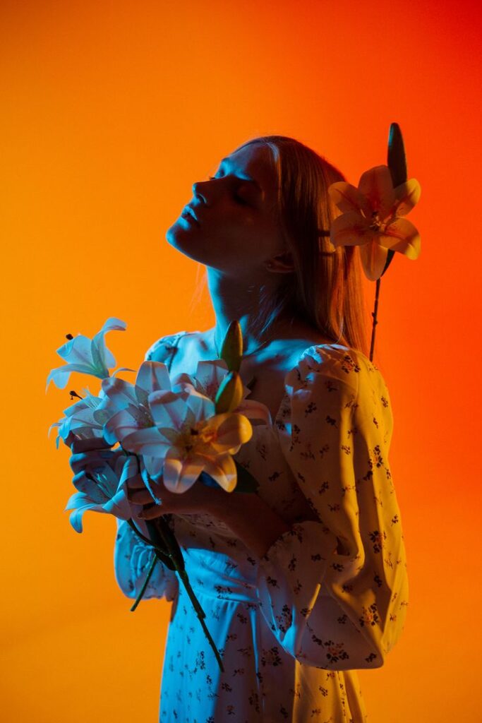 hhh_ney - Handy Home Woman in floral dress holding lilies, with vivid orange and blue background, showcasing artistic expression and color contrast.