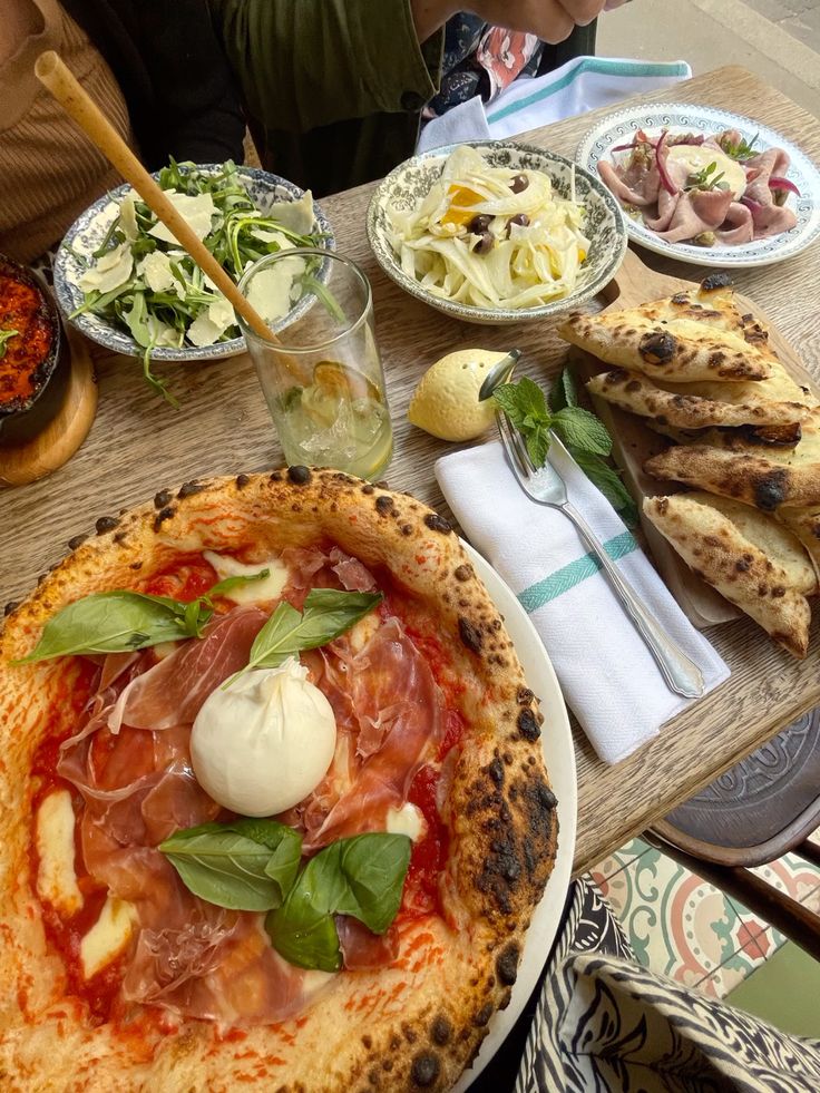 italy food pizza - Handy Home Delicious Italian spread with prosciutto pizza, fresh salads, and bread on a rustic wooden table, perfect for a gourmet meal.