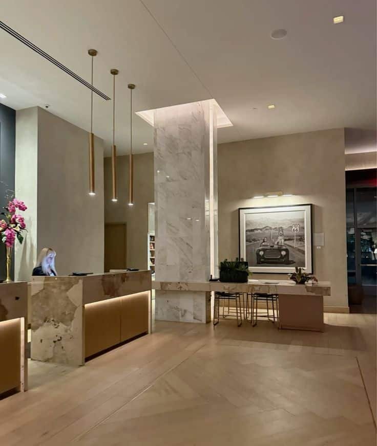 Modern hotel lobby with marble accents, reception desk, and Route 66 artwork, featuring warm lighting and elegant decor.