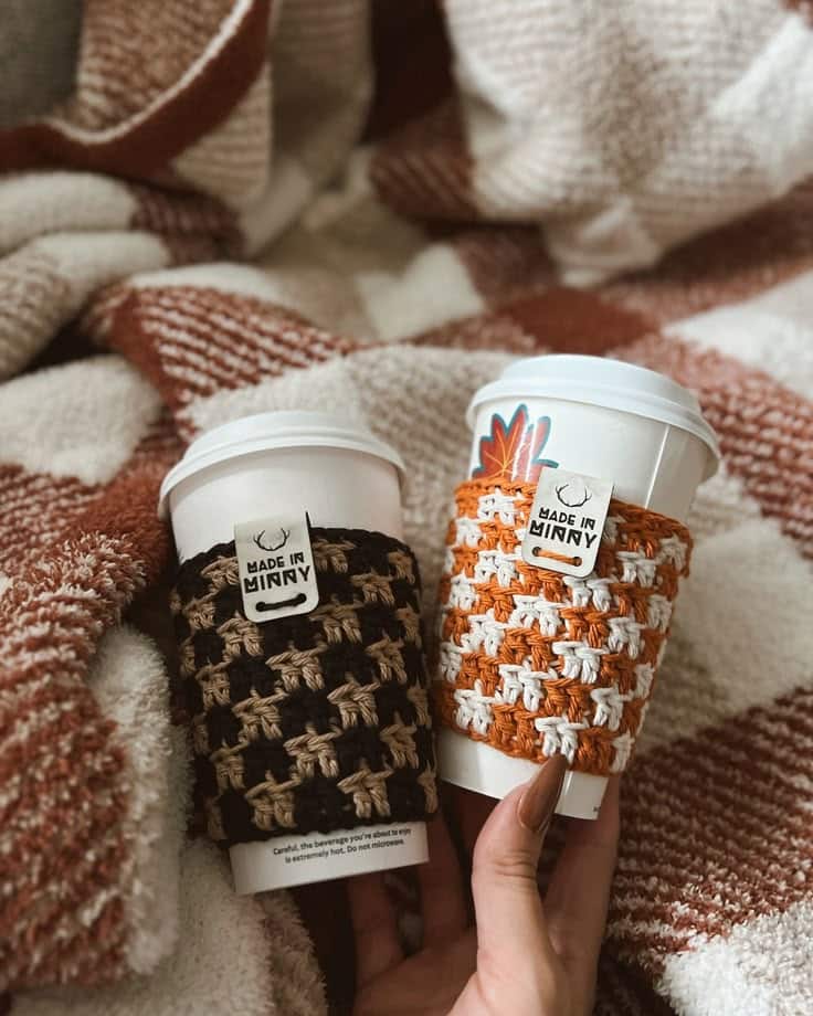 Cozy coffee cups with handmade knitted sleeves in warm hues on a soft blanket, perfect for fall mornings and autumn vibes.