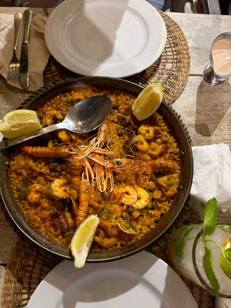 paella 🥘 - Handy Home Seafood paella served in a pan with fresh prawns, lemon wedges, and a side of drink on a rustic table setting.