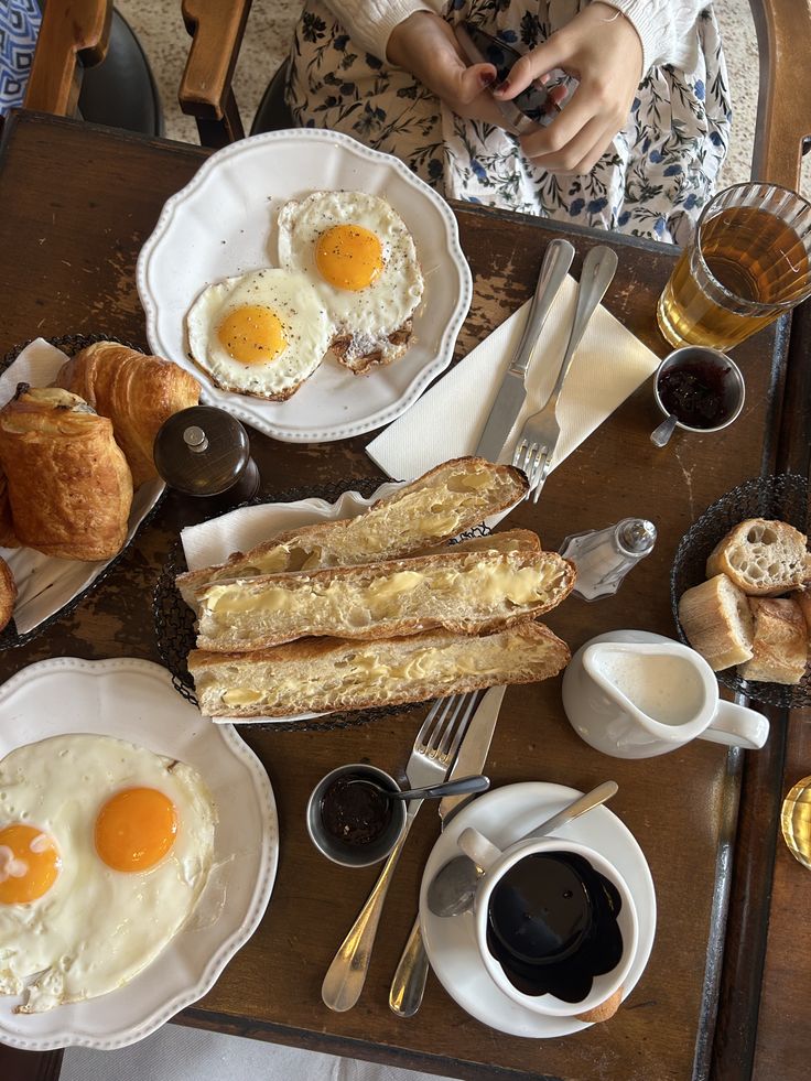 paris food france aesthetic - Handy Home Delicious breakfast spread with sunny-side-up eggs, croissants, baguettes, jam, and coffee on a rustic wooden table.