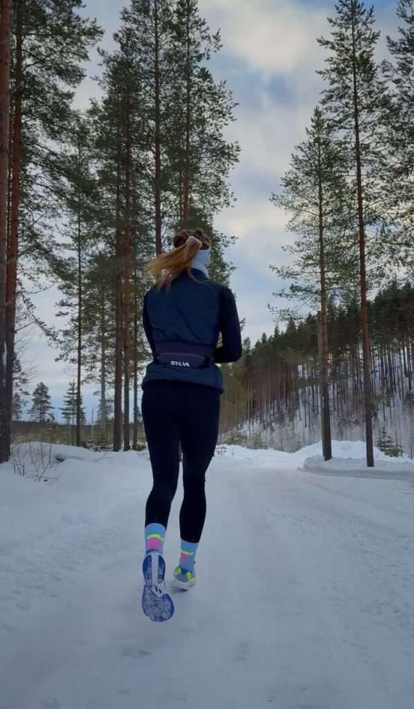 Person jogging on a snowy forest trail, wearing winter running gear, vibrant socks, and snow-covered shoes. Winter fitness concept.