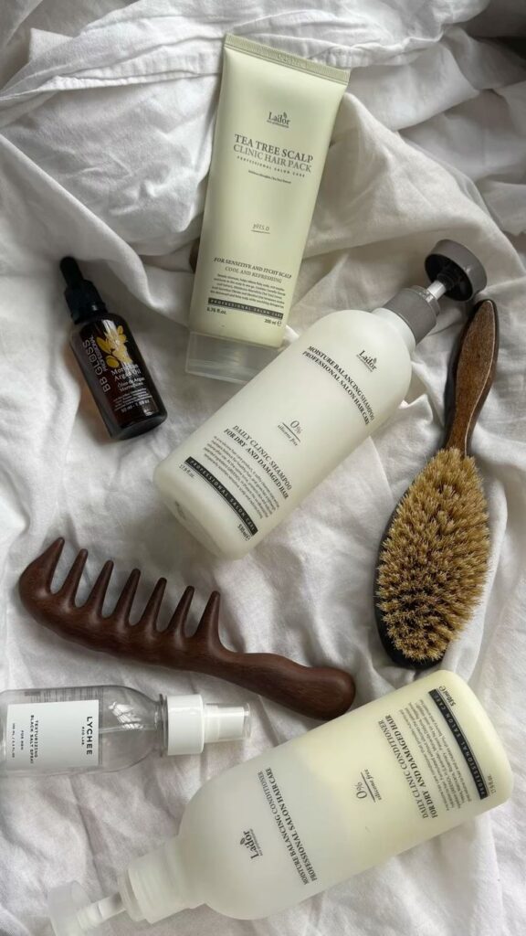 sgbae - Handy Home Hair care products with a wooden comb and brush on white fabric. Includes Tea Tree Scalp Hair Pack, conditioner, serum, and spray.