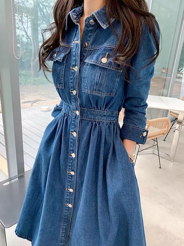 Woman in a stylish denim dress with buttons, standing indoors near a window. Perfect for casual or chic outfits.