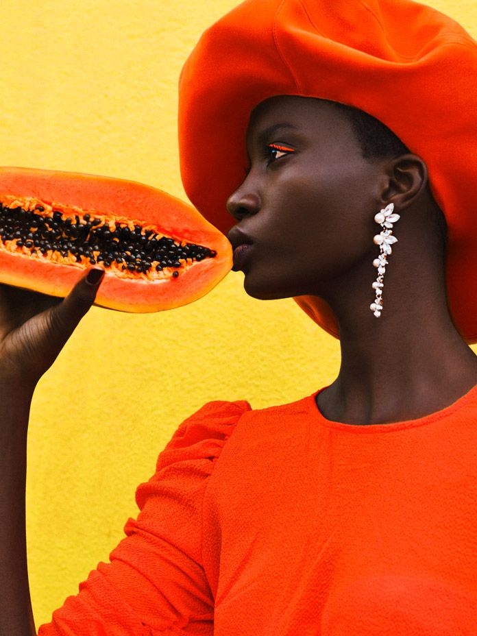 undefined - Handy Home Fashionable person in orange attire holding a papaya against a vibrant yellow background, showcasing bold style and elegance.