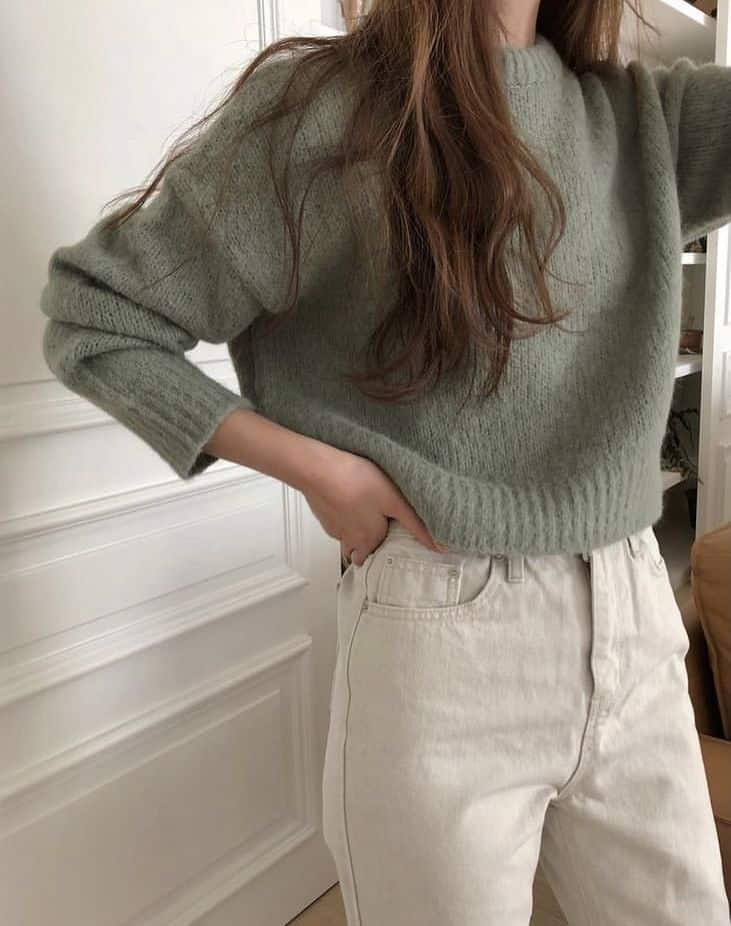 Woman wearing a cozy green sweater and high-waisted white jeans in a stylish indoor setting. Fashion and style concept.