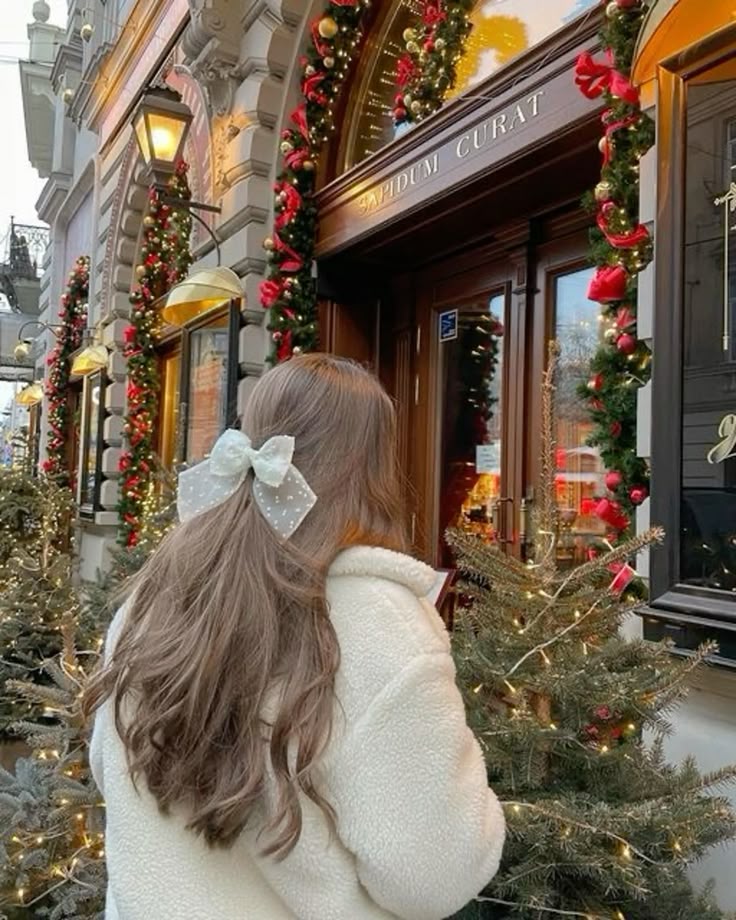 Woman in winter coat with bow admires festive Christmas decorations and lights outside a shop.