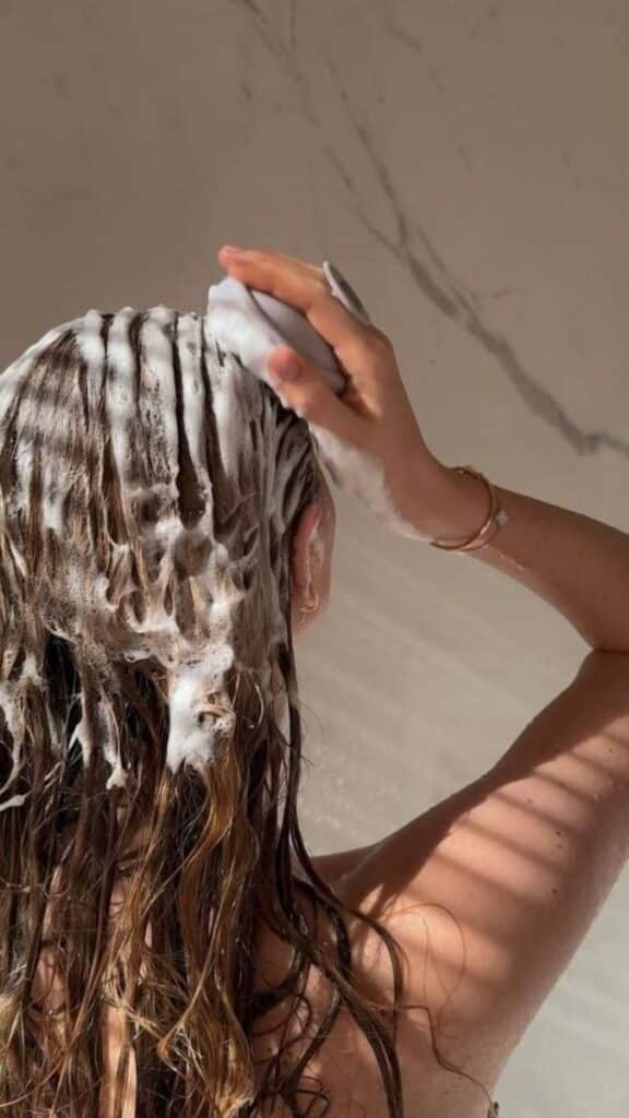 zdgb - Handy Home Person washing hair with shampoo, creating lather and foam in a shower setting. Haircare routine, self-care concept.