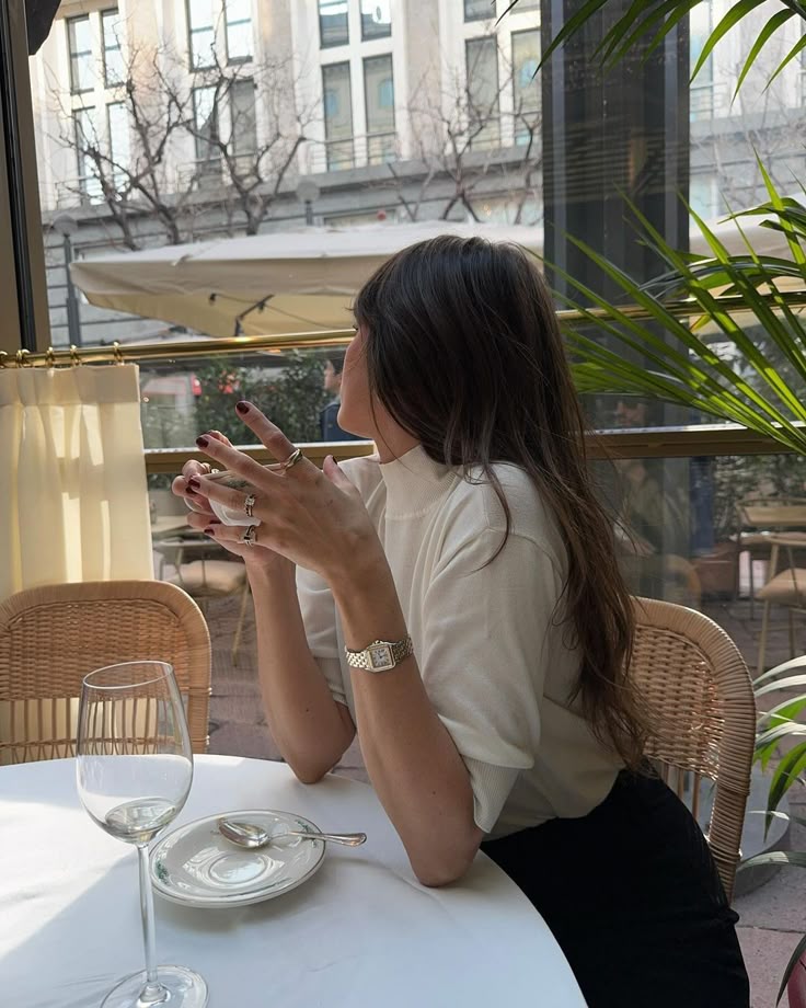 zgbnzdfbd - Handy Home Woman enjoying a drink at an outdoor café, wearing a white top and jewelry, with urban background and greenery.