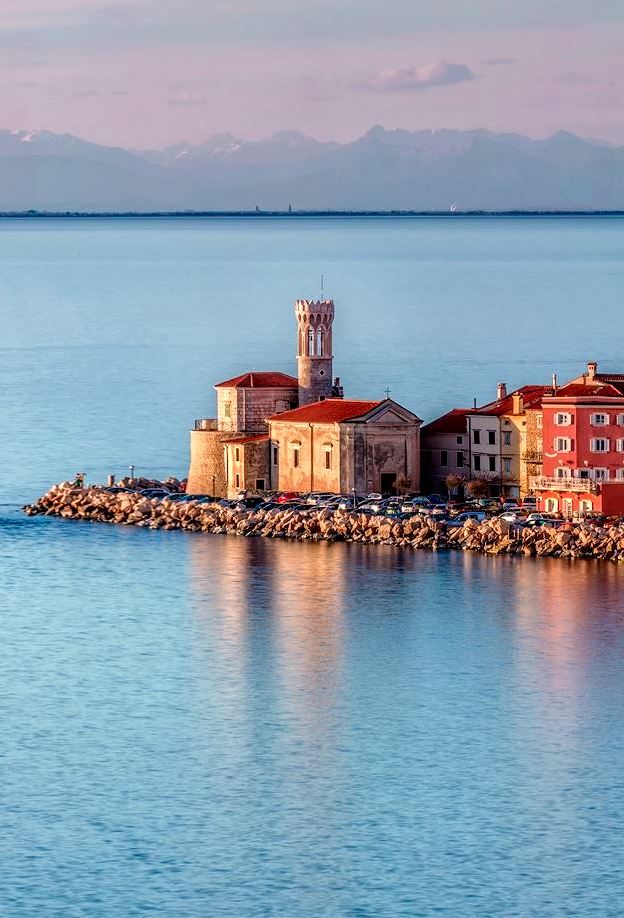 ыяпияви - Handy Home Historic waterfront buildings in Izola, Slovenia, with calm sea and distant mountains at sunset, creating a serene coastal scene.
