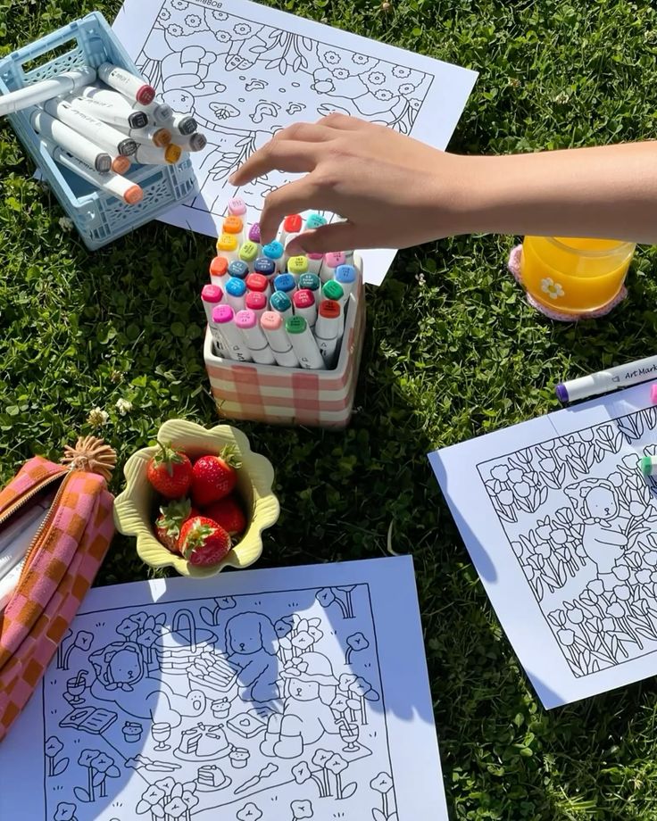 Coloring session outdoors with markers, strawberries, and coloring sheets on green grass. Creative fun in nature.
