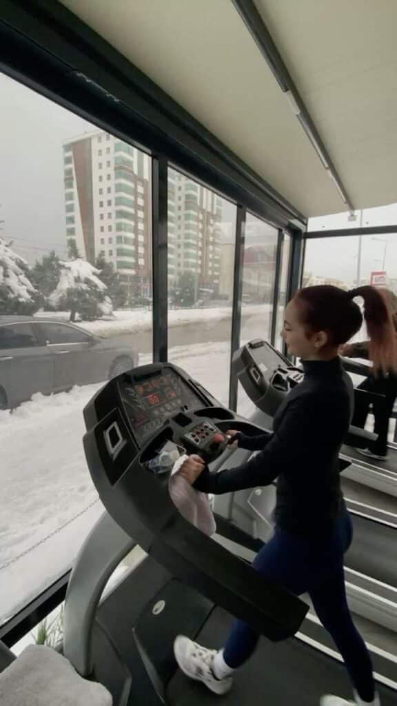 Person running on treadmill by snowy window, enjoying winter workout indoors at gym.
