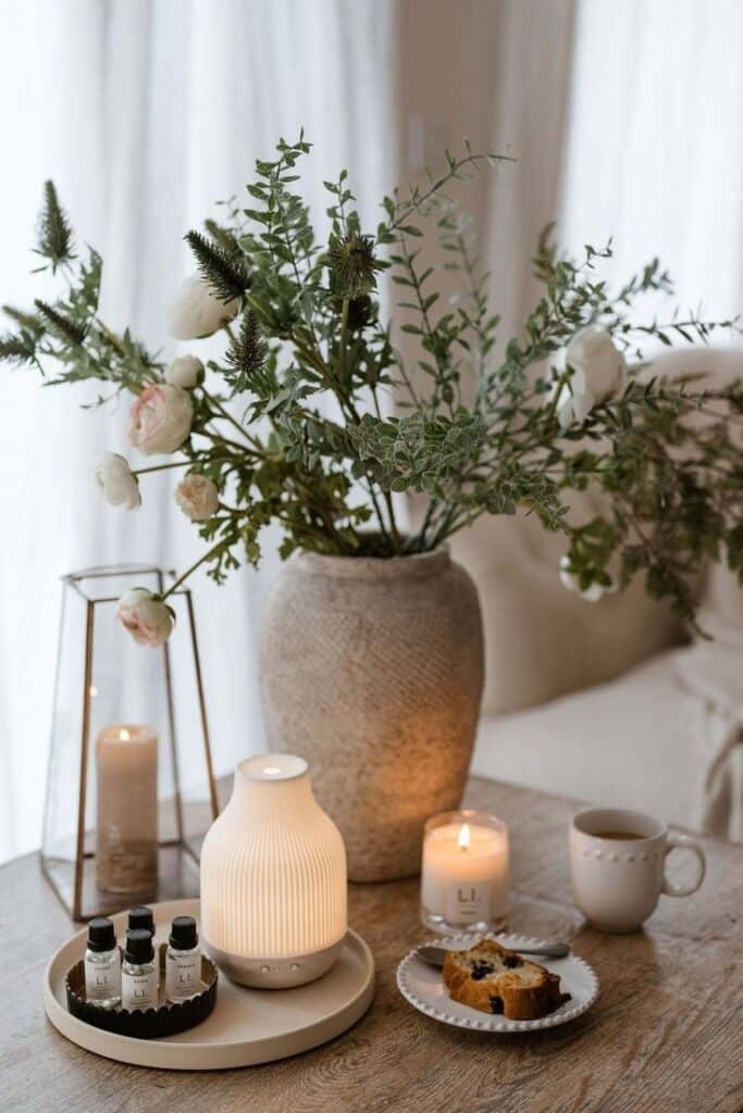 0794ca8b-a278-4bd0-98b8-998b72009ce8 - Handy Home Cozy room decor with a vase of flowers, diffuser, candles, and tea on a wooden table. Perfect serene atmosphere.