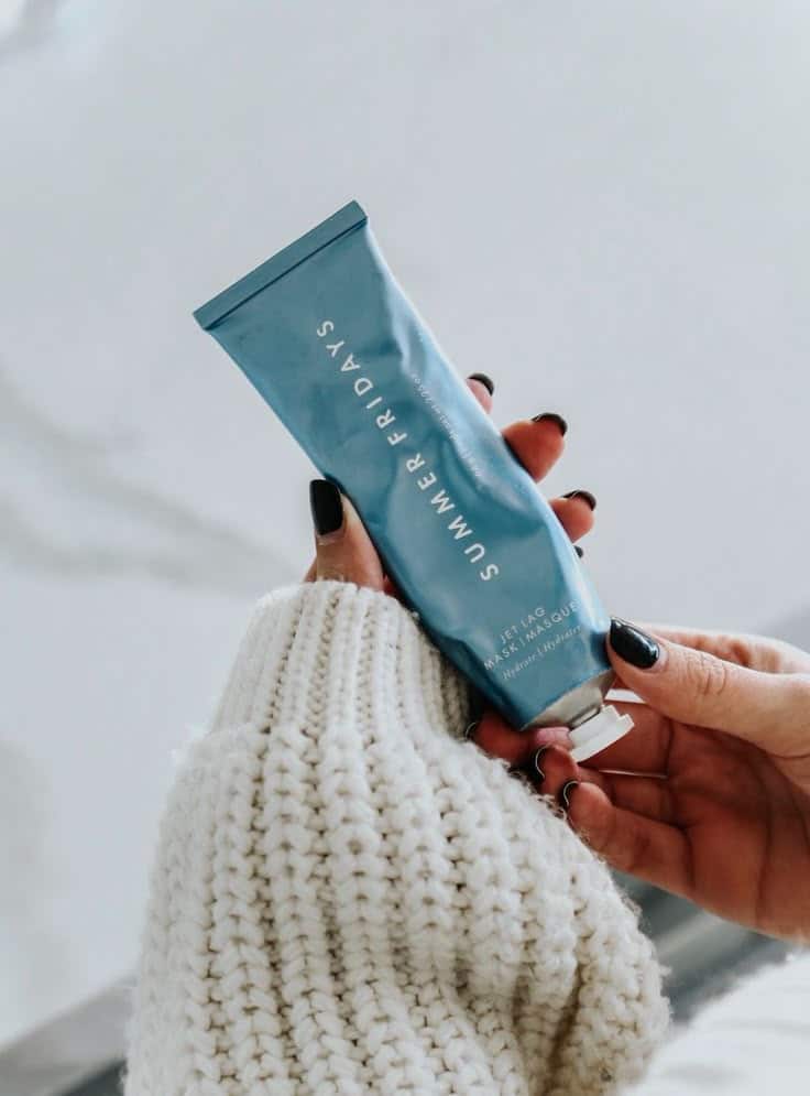 10 Beauty Products To Get Your Skin Through Winter - Somewhere Lately - Handy Home Person holding a tube of Summer Fridays Jet Lag Mask with manicured nails and cozy sweater.